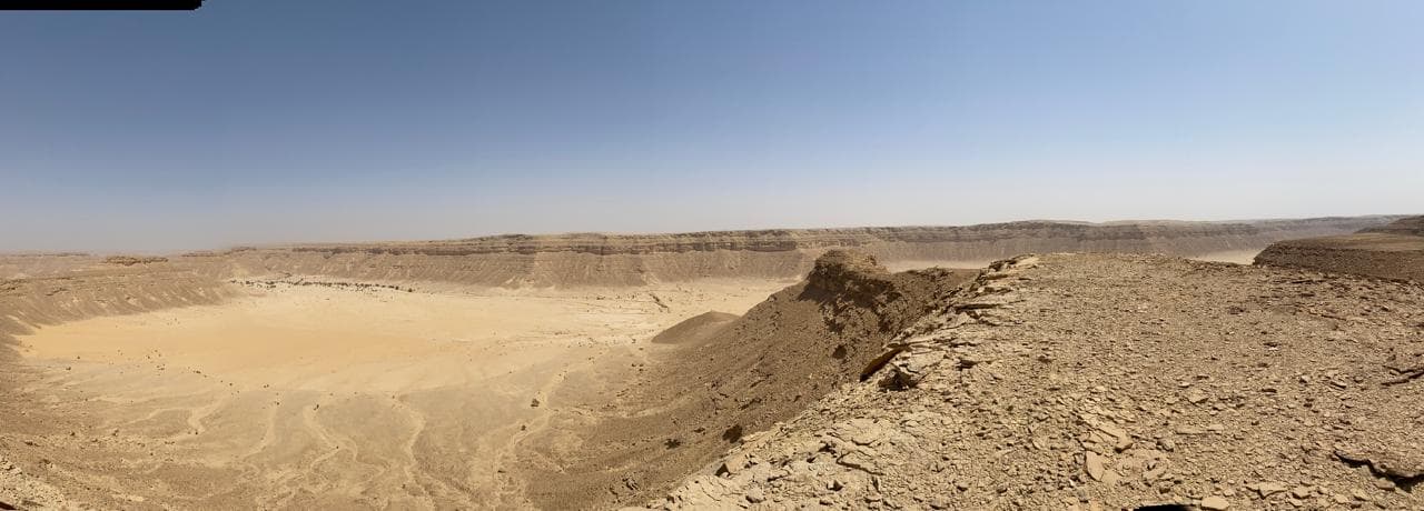 An eroded desert escarpment enclosing a broad sand-floored basin