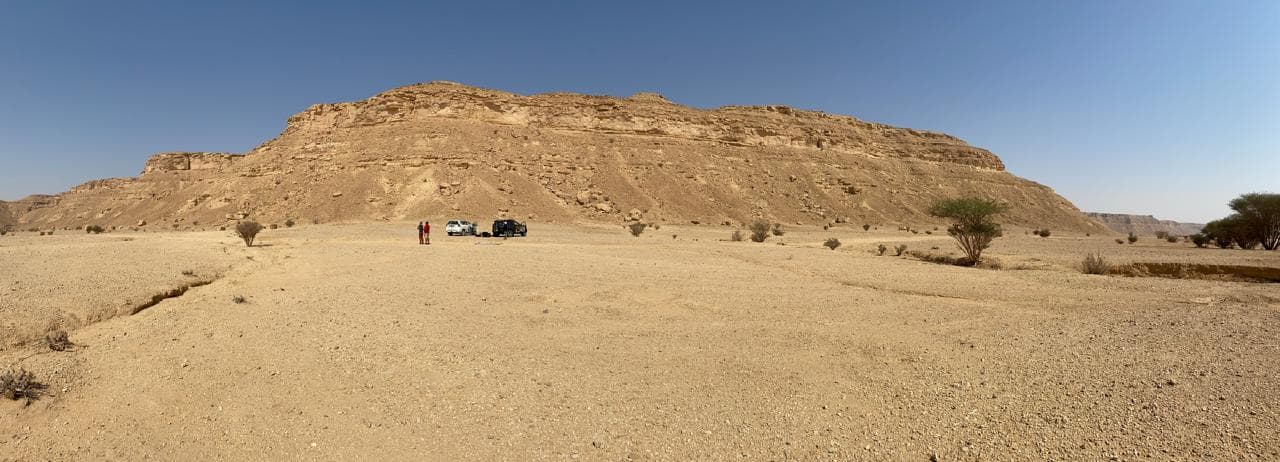 Field vehicles parked on a gravel plain below a flat-topped desert butte